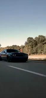 Black car driving on open road with trees in background.
