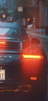 A sleek car with glowing taillights on a rainy city street at night.