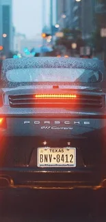 Sleek car driving through a rainy city street with glowing tail lights.