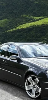 Sleek black car on a scenic mountain road with lush green hills.