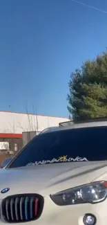 Luxury white car under clear blue sky with trees.