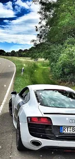 Sleek white car on a scenic countryside road with lush greenery and blue sky.