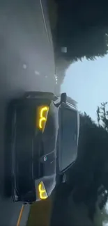 Sleek black car with yellow headlights driving on a misty road at night.