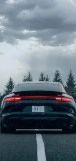 Sleek car with glowing tail lights on an expansive road under a dramatic sky.