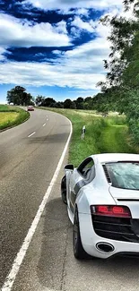 White sports car on a scenic country road under a blue sky with lush greenery.