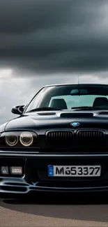 Sleek black car parked under a dramatic, stormy sky on the road.