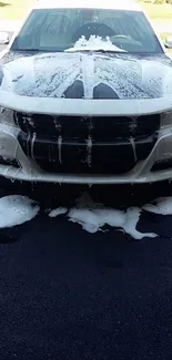 White car covered with soap suds during wash on driveway.