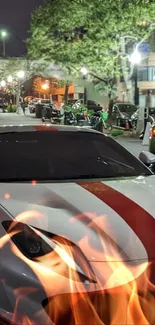 White sports car on a city street at night with red flames in the foreground.