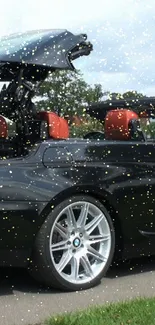 Black convertible car with open top and golden sparkles on the road.