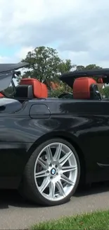 Sleek black convertible car with red leather interiors parked on a scenic road.