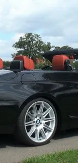 Black convertible with red interior on a scenic road.