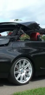 Black convertible car with red interior against a cloudy sky backdrop.