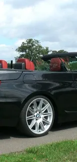 Sleek black convertible car with a red interior, parked on a sunny day.