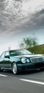 Sleek green car driving fast on a highway against dramatic clouds.