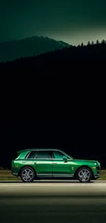 Green SUV on dark road with mountains at night.