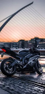 Black motorcycle by a bridge with sunset reflecting on water.