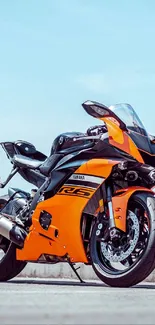 Vibrant orange motorcycle parked on open road under clear blue sky.