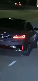 Sleek black car driving at night with glowing taillights.