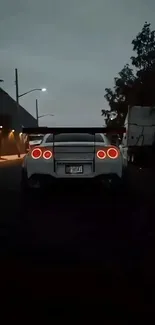 White sports car with glowing tail lights at night.