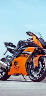 Vibrant orange motorcycle on concrete against a clear sky.