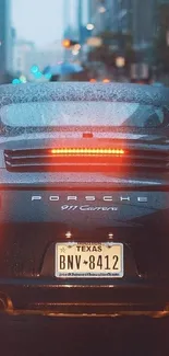 Porsche 911 Carrera driving in rainy city at night.