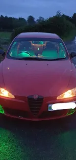 Red car with green lights on a nighttime road.