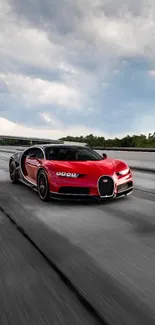 Red sports car on highway under cloudy sky.