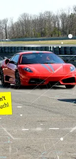 Red sports car on racetrack with 'Don't Touch!' sign.