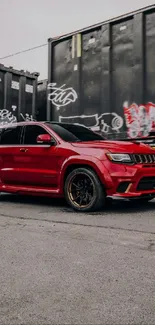 Red SUV by graffiti-covered cargo containers.