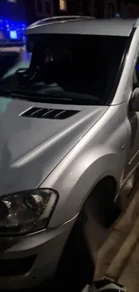 Sleek silver car parked under city lights at night.