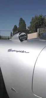 Sleek silver Spyder car side view with blue sky backdrop.