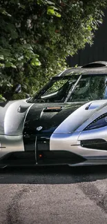 Sleek silver supercar parked by foliage and brick wall.