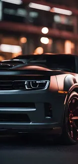 Sleek grey sports car in city at night, glowing under bright lights.