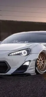 Sleek white sports car with custom rims on a road at sunset.