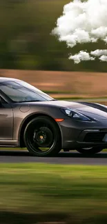 Sleek gray sports car on a race track with greenery in the background.