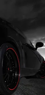 Sleek black sports car with red rims against a dramatic dark sky.