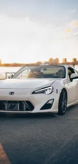 Sleek white sports car driving on city road at sunset.