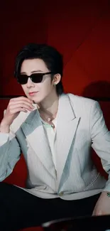 Stylish individual in sunglasses against a red background.