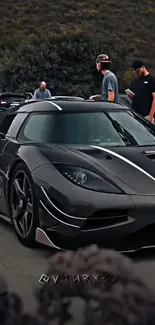 Sleek black supercar parked on street with people around.