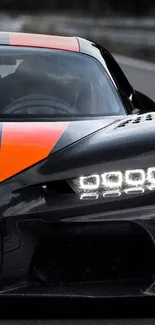 Sleek black sports car with orange racing stripes on the road.