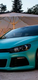 Sleek turquoise sports car with chrome wheels under white umbrella.