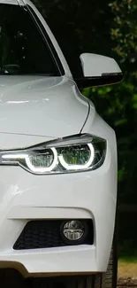 Sleek white car with shining headlights against a leafy background.