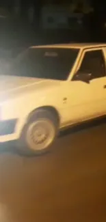 Vintage white car driving at night with headlights on.