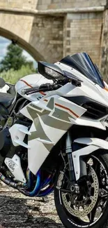 Sleek white motorcycle by a stone bridge.