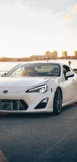 Sleek white sports car on urban road with cityscape backdrop.