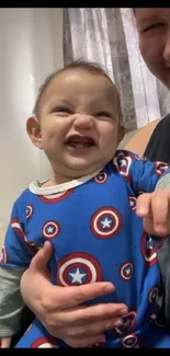 Smiling baby wearing a blue onesie with playful patterns.