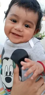 Smiling baby in Disney-themed outfit outdoors.