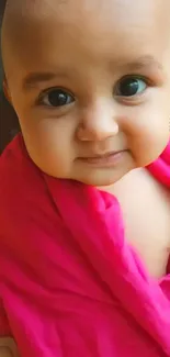 Smiling baby wrapped in a vibrant pink blanket on mobile wallpaper.