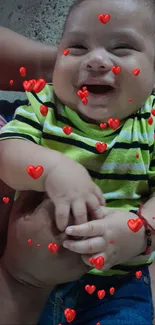 Smiling baby wearing a green striped shirt, being held lovingly.