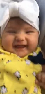 Smiling baby wearing a yellow dress and white bow, radiating joy.